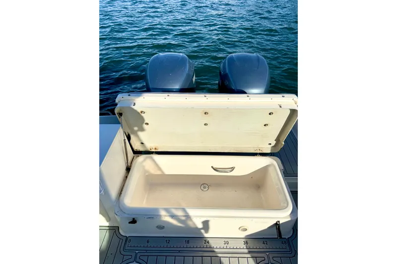 Slide: The Image of 2003 Pursuit 2870 Walkaround boat with open storage compartment and twin engines on water. - 10