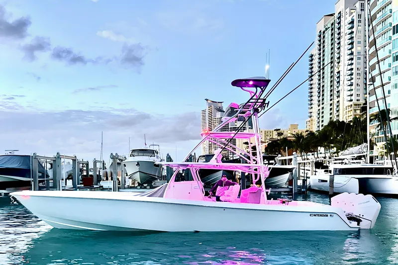 The Image of 2024 Contender 44 ST boat with pink lighting docked in a marina, city skyline background. - 0