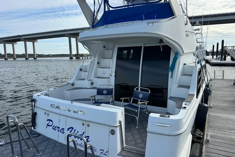 Slide: The Image of 2005 Carver 36 Super Sport yacht docked, featuring spacious deck and seating, near a bridge. - 13