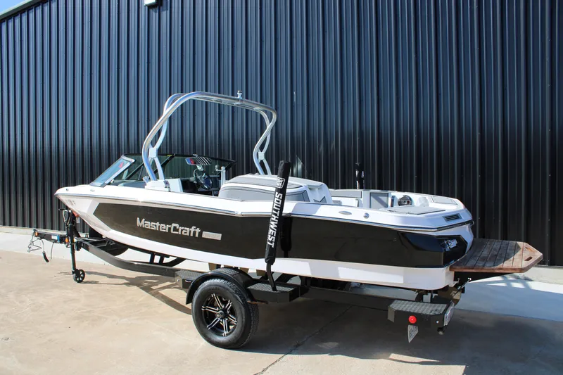 Slide: The Image of 2022 MasterCraft ProStar boat on trailer, parked by black metal wall. - 2