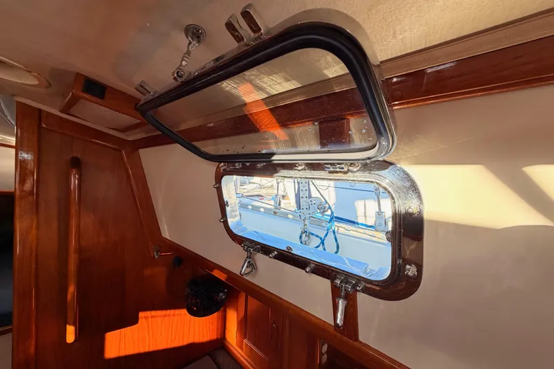 Slide: The Image of Interior view of a 1995 Pacific Seacraft 34 sailboat, featuring a wooden cabin and open porthole. - 60