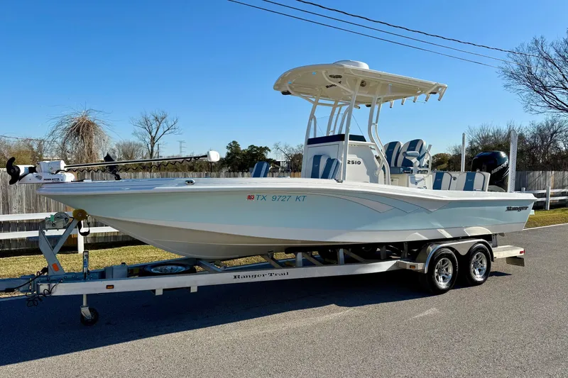The Image of 2022 Ranger 2510 Bay boat on trailer, parked outdoors under clear blue sky. - 1