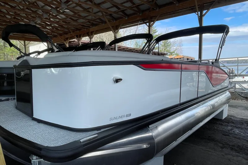 The Image of 2026 Harris Sunliner 230 pontoon boat under a wooden shelter by the lake. - 0