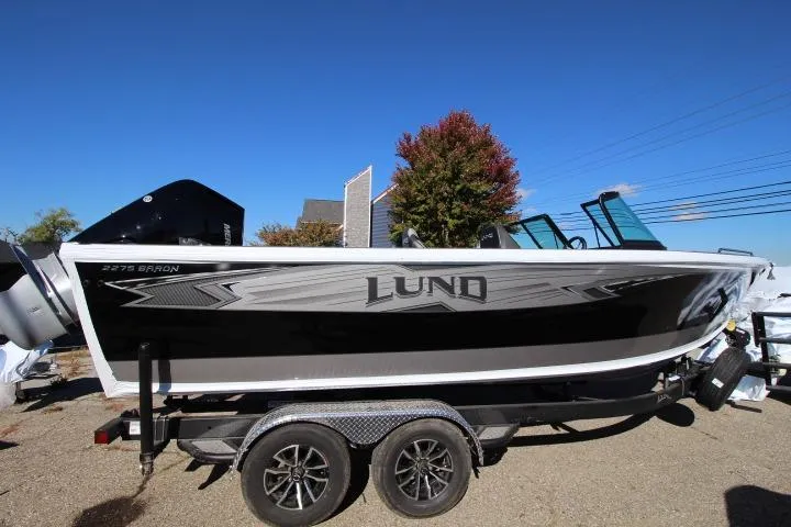 The Image of 2026 Lund 2275 Baron boat on trailer, side view, under clear blue sky. - 0