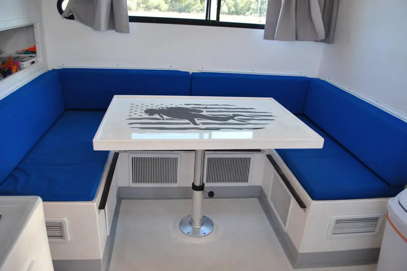 Slide: The Image of Interior of 2019 Newton 53 dive boat with blue seating and diver-themed table. - 16