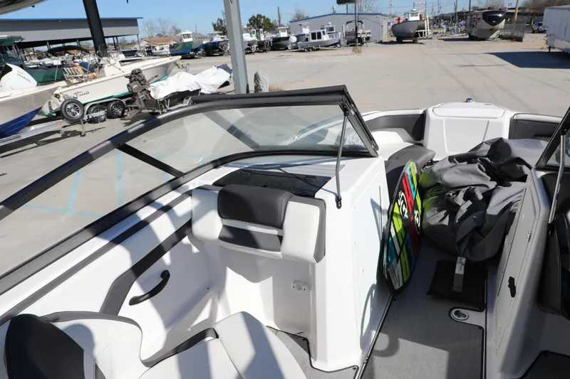 Slide: The Image of 2022 Yamaha Boats AR210 interior with seating and storage, parked in a marina. - 11
