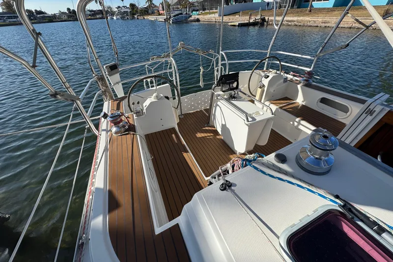 Slide: The Image of 2006 Shannon Shoalsailer sailboat deck with wooden flooring and steering wheel, docked by the water. - 4