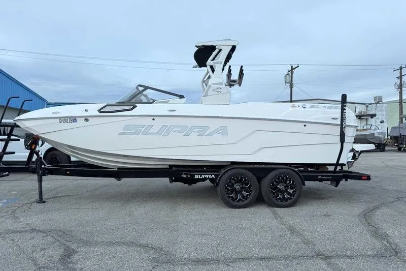 The Image of 2022 Supra SL boat on trailer, white exterior, parked outdoors. - 1