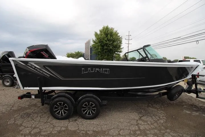 Slide: The Image of 2026 Lund 2075 Fisherman boat on trailer, sleek black design, parked outdoors. - 1
