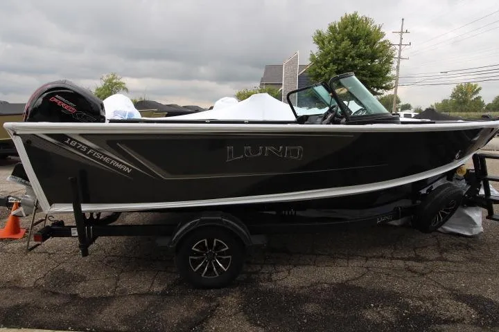 The Image of 2026 Lund 1875 Fisherman boat on trailer, parked outdoors on a cloudy day. - 0