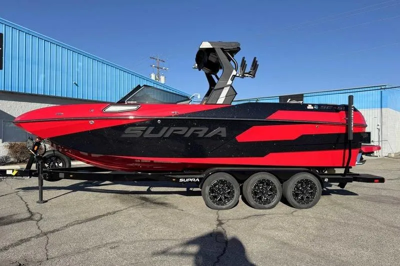 The Image of 2025 Supra SE boat in red and black on a trailer, parked outdoors. - 1