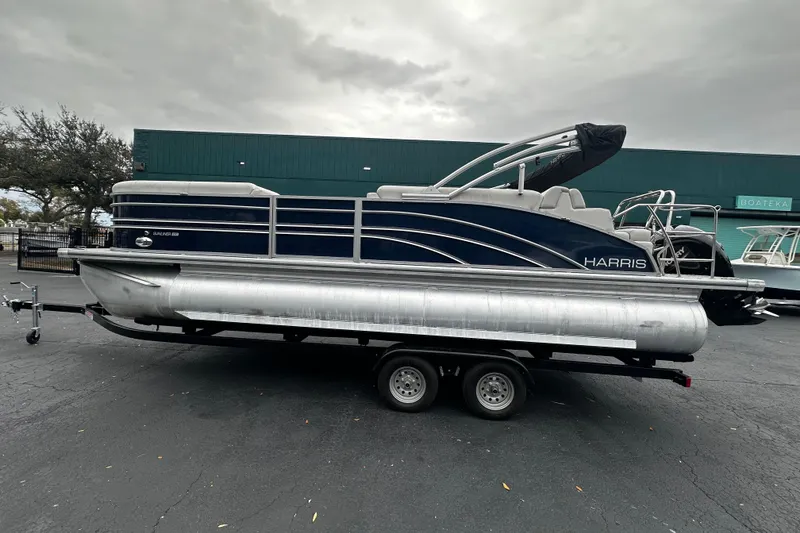 Slide: The Image of 2025 Harris Sunliner 230 pontoon boat on trailer, parked outdoors. - 2