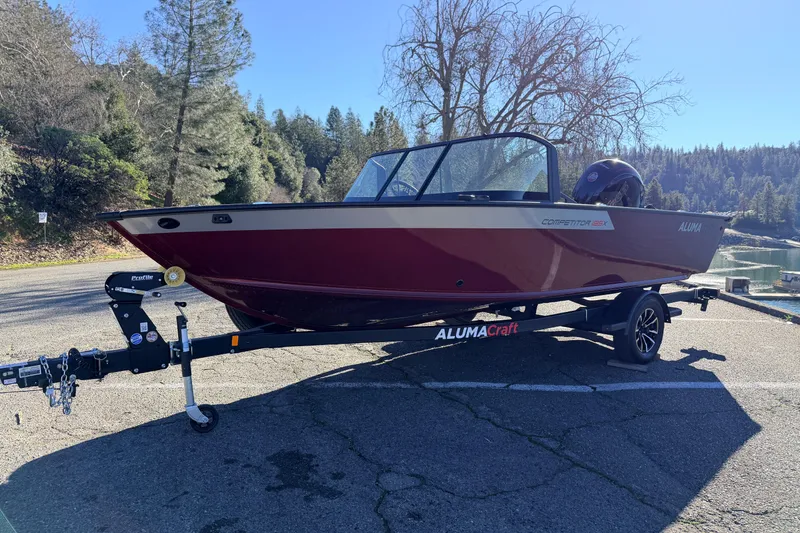 Slide: The Image of 2025 Alumacraft Competitor 185X Sport boat on trailer, parked near scenic lake. - 10
