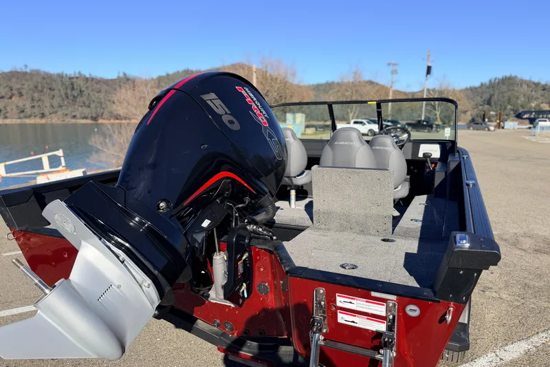 Slide: The Image of 2025 Alumacraft Competitor 185X Sport boat with powerful 150 HP engine, docked by a lake. - 16