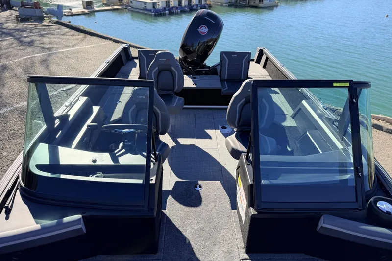 Slide: The Image of 2025 Alumacraft Competitor 185X Sport boat interior with seating and windshield, docked by the water. - 20