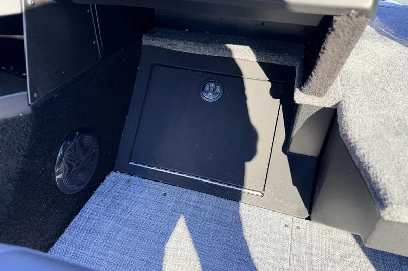 Slide: The Image of 2025 Alumacraft Competitor 185X Sport interior storage compartment with speaker and carpeted flooring. - 37