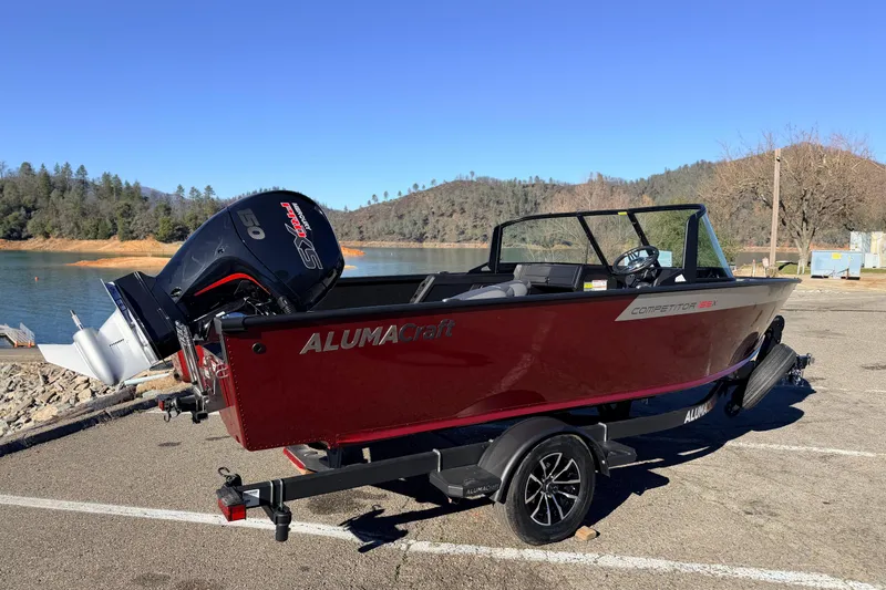Slide: The Image of 2025 Alumacraft Competitor 185X Sport boat on trailer by a scenic lake. - 7