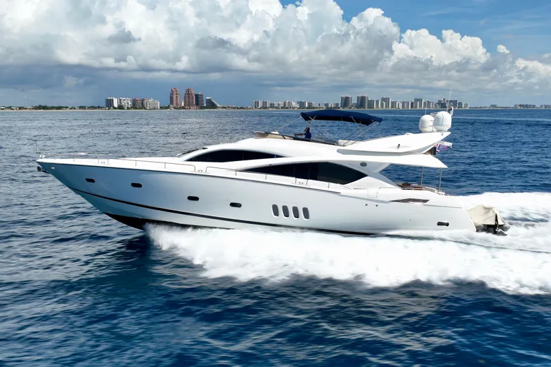 Slide: The Image of 2005 Sunseeker 82 Yacht cruising on open water with city skyline in background. - 2