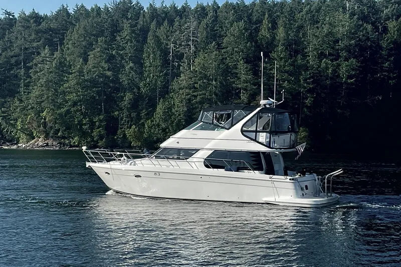 The Image of 2000 Carver 450 Voyager Pilothouse yacht cruising on a serene lake with forested backdrop. - 0
