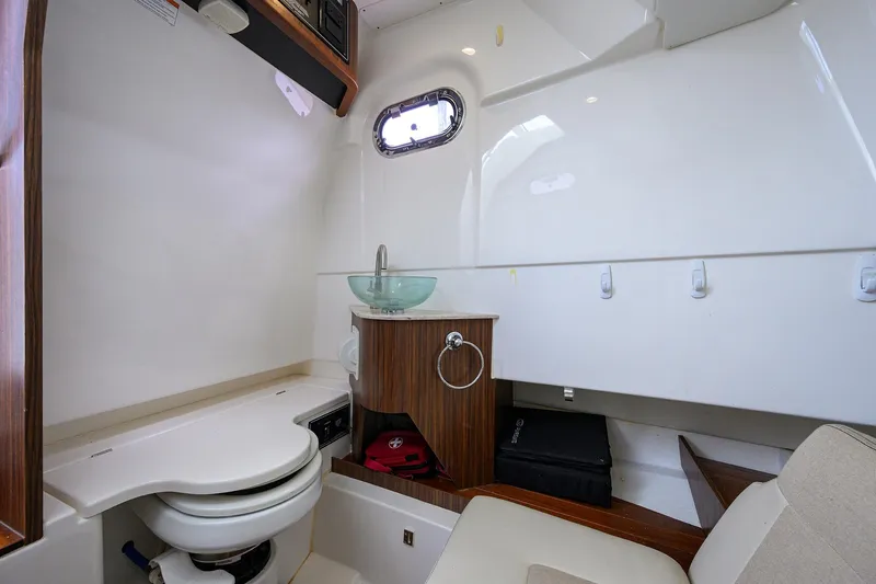 Slide: The Image of 2019 Pursuit S 328 Sport boat interior with toilet, sink, and wooden cabinetry. - 31