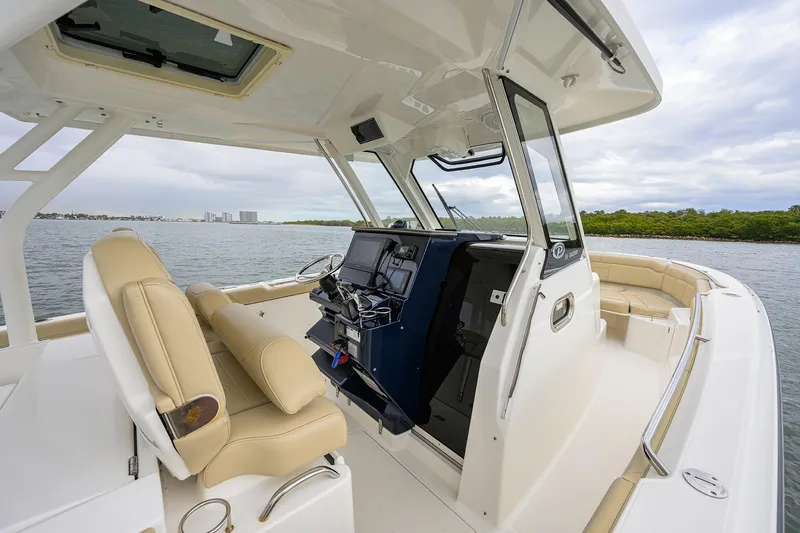 Slide: The Image of 2019 Pursuit S 328 Sport boat interior with helm, beige seating, and ocean view. - 55