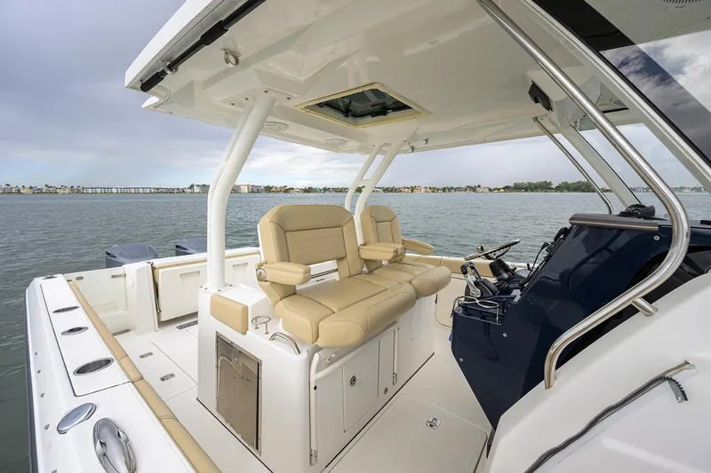 Slide: The Image of 2019 Pursuit S 328 Sport boat interior with beige seating and helm, on calm water. - 58