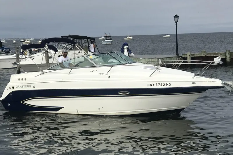 The Image of 2007 Glastron GS 279 boat docked on a calm waterfront with other boats nearby. - 0