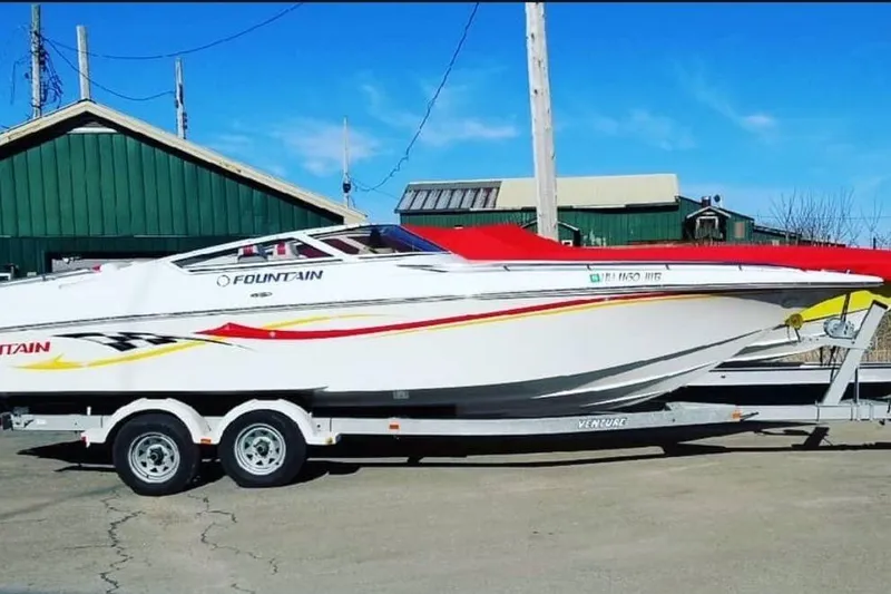 The Image of 2005 Fountain 27 Fever speedboat on trailer, parked outdoors under clear blue sky. - 1