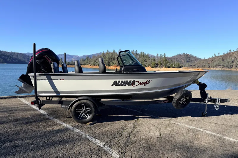 The Image of 2024 Alumacraft Competitor 175X Sport boat on trailer by a scenic lake. - 1