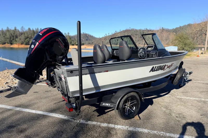Slide: The Image of 2024 Alumacraft Competitor 175X Sport boat on trailer by a scenic lake. - 2