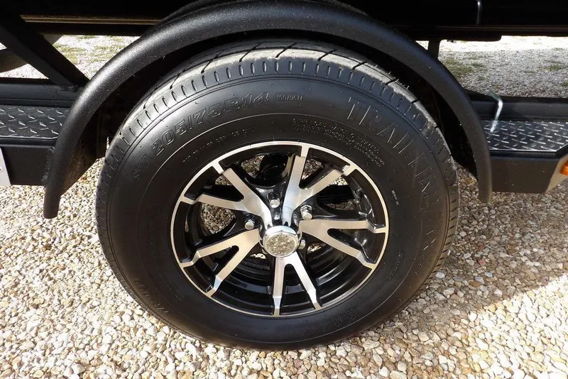 Slide: The Image of 2026 Crestliner XF 189 trailer wheel with black and silver alloy rim on gravel. - 39