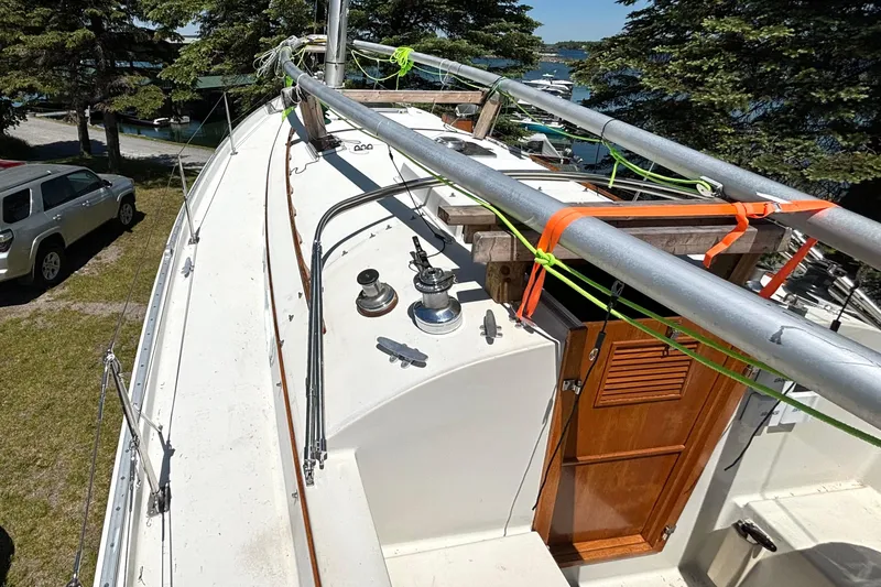 Slide: The Image of 1985 Nonsuch 30 Ultra sailboat deck with winches and wooden hatch, docked near trees. - 19