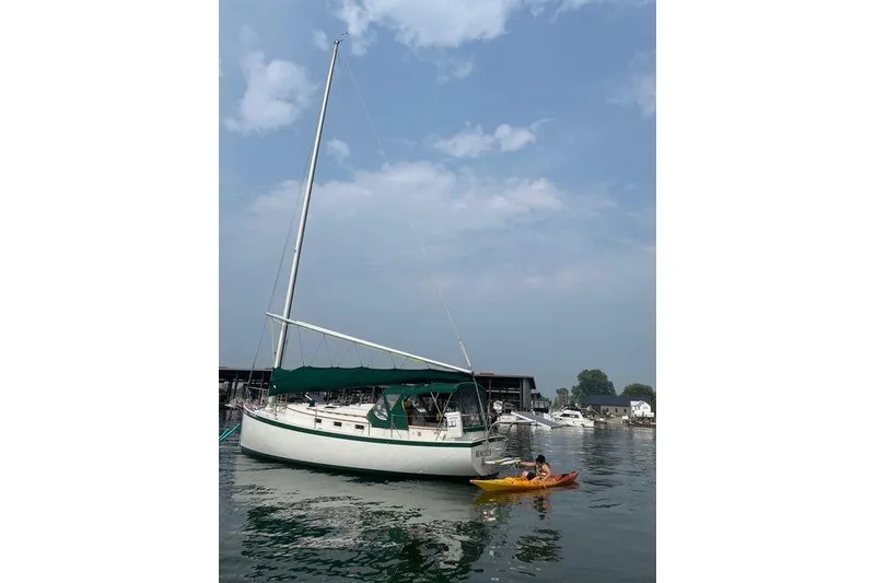 Slide: The Image of 1985 Nonsuch 30 Ulta sailboat with green canopy on calm water, kayaker nearby. - 2