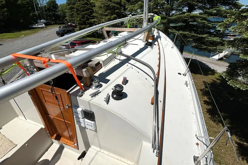 Slide: The Image of 1985 Nonsuch 30 Ultra sailboat deck with winches and wooden hatch, surrounded by trees. - 21