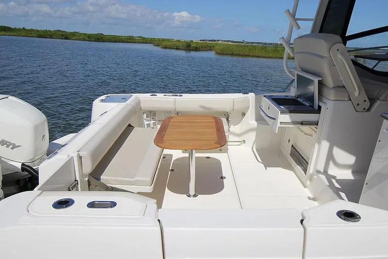 Slide: The Image of Manufacturer Provided Image: Boston Whaler 325 Conquest 2026 boat deck with seating and table, overlooking serene water. - 10
