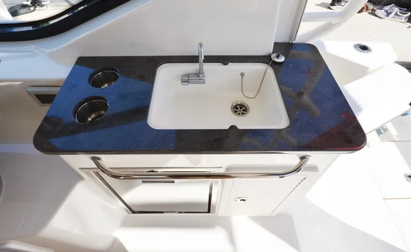 Slide: The Image of Manufacturer Provided Image: 2026 Boston Whaler 325 Conquest boat sink with black countertop and storage cabinet. - 9
