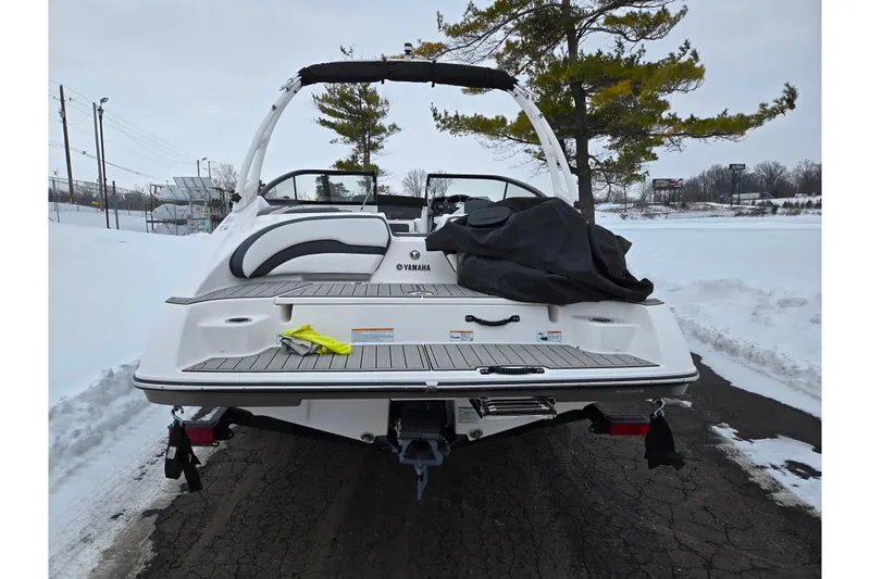 Slide: The Image of 2023 Yamaha Boats AR195 on snowy road, rear view with cover and trees. - 2
