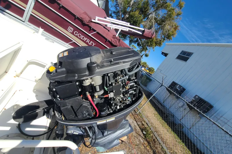 Slide: The Image of 1995 Mako 201 Center Console boat engine, outdoor setting, near a maroon Godfrey boat. - 16