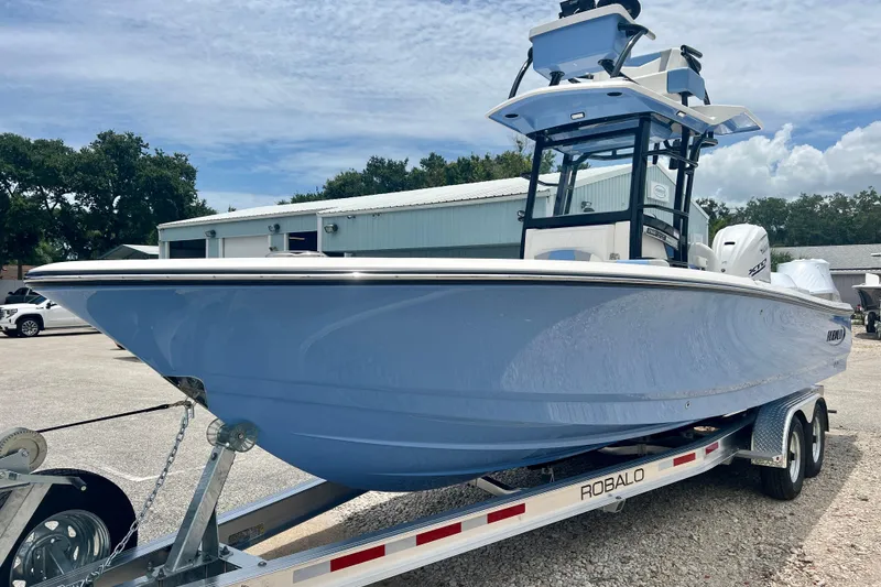 Slide: The Image of 2025 Robalo 266 Cayman SD boat on trailer, parked outdoors under a cloudy sky. - 2