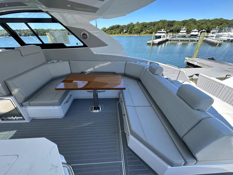 Slide: The Image of 2024 Cruisers Yachts 42 GLS Outboard, spacious seating area with a wooden table, docked at a marina. - 13