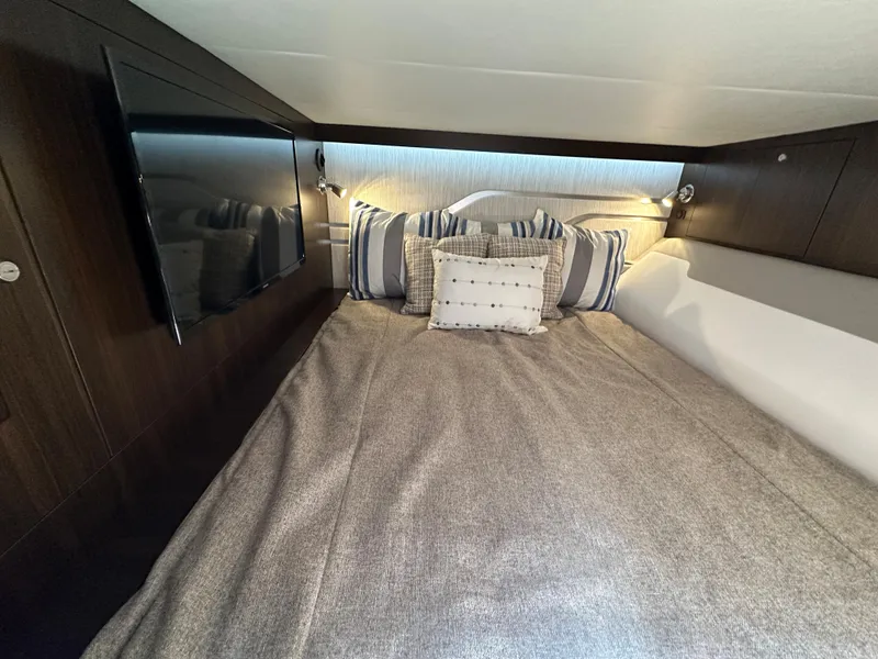 Slide: The Image of 2024 Cruisers Yachts 42 GLS Outboard cabin with cozy bed, pillows, and wall-mounted TV. - 27