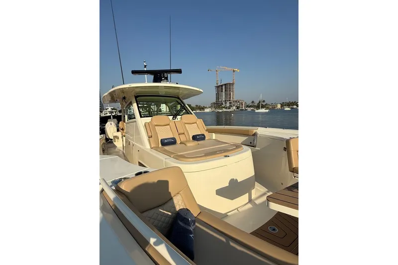Slide: The Image of 2024 Scout 400 LXF luxury boat with tan seating, docked by waterfront buildings. - 6