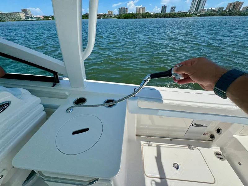 Slide: The Image of 2025 Robalo R257 Dual Console boat interior with hand holding a shower hose, ocean view. - 25