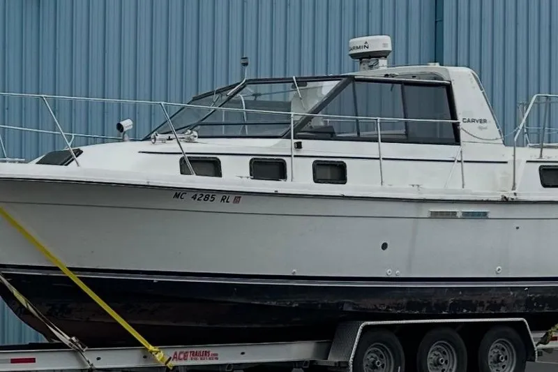 Slide: The Image of 1985 Carver 28 Riviera boat on trailer, parked near blue building. - 3