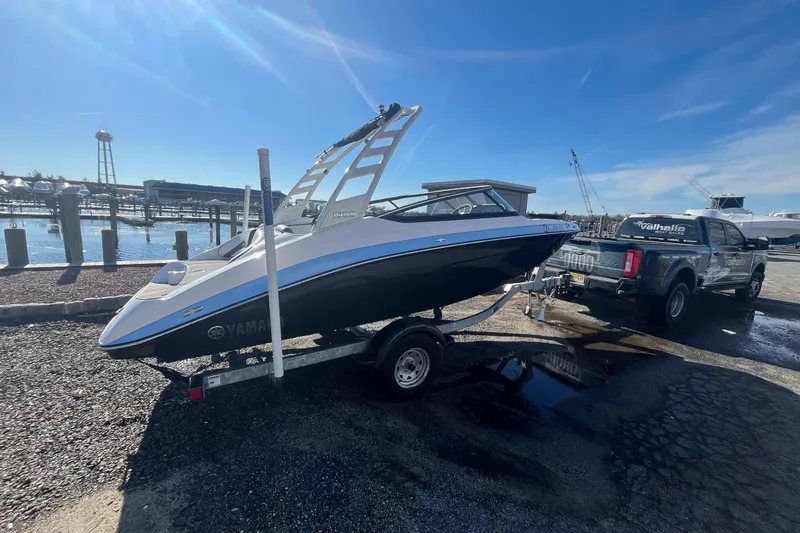 Slide: The Image of 2025 Yamaha Boats 195S on trailer, parked near waterfront under clear blue sky. - 3