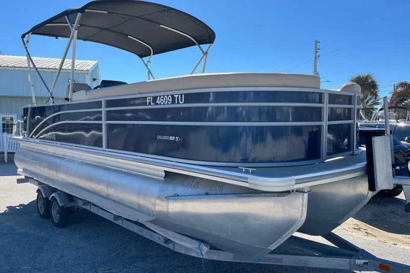 The Image of 2024 Harris Cruiser 230 pontoon boat on trailer, featuring sleek design and canopy. - 0