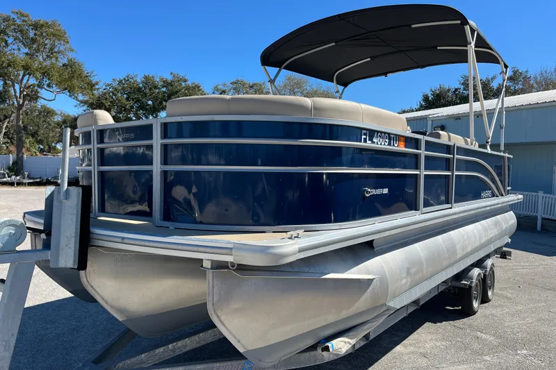 Slide: The Image of 2024 Harris Cruiser 230 pontoon boat on trailer, parked outdoors under clear sky. - 2