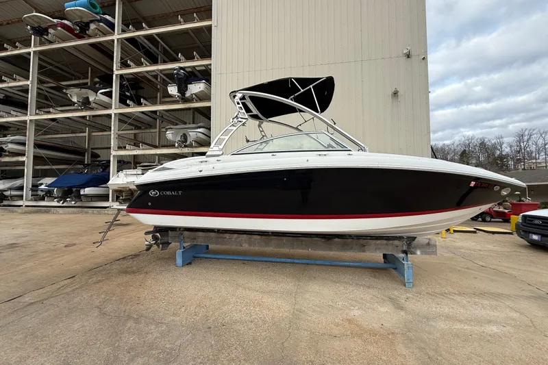 The Image of 2011 Cobalt 242 boat in storage, black hull with red stripe, outdoor facility. - 1