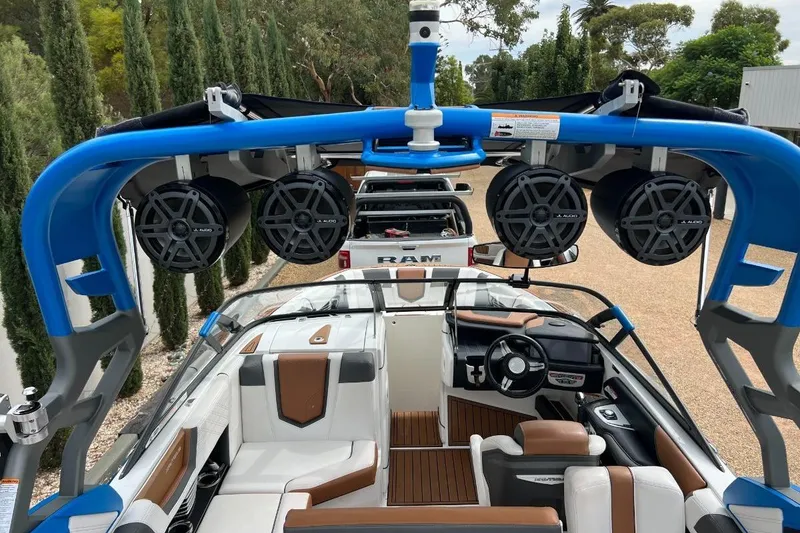 Slide: The Image of 2018 Nautique Super Air Nautique G23 boat interior with speakers and seating, parked near trees. - 8