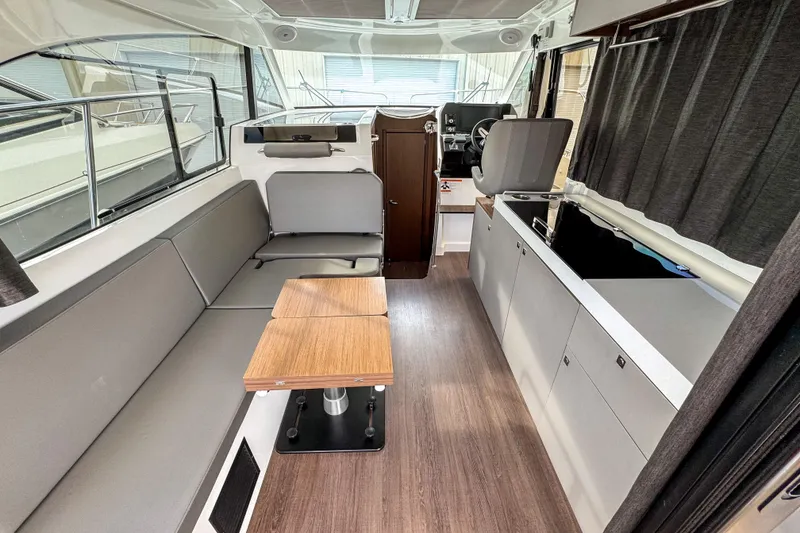 Slide: The Image of 2024 Beneteau Antares 11 interior with modern seating, wooden table, and sleek kitchen area. - 10